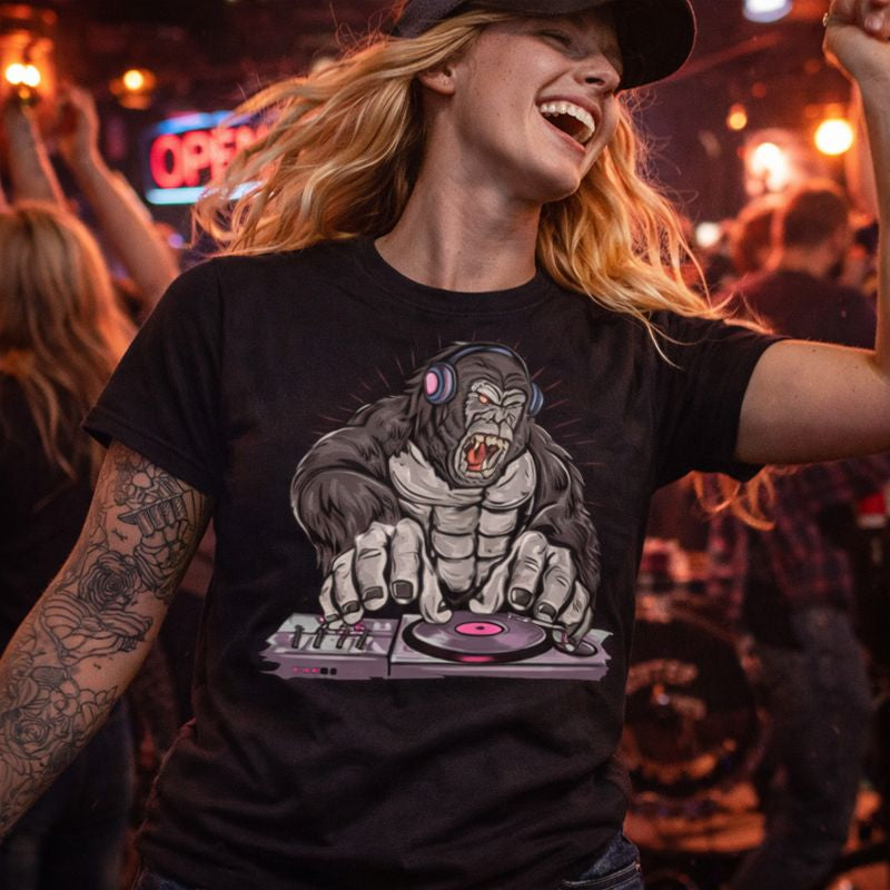 Person wearing a black t-shirt with a graphic design of a gorilla on a turntable, standing in a lively crowd.