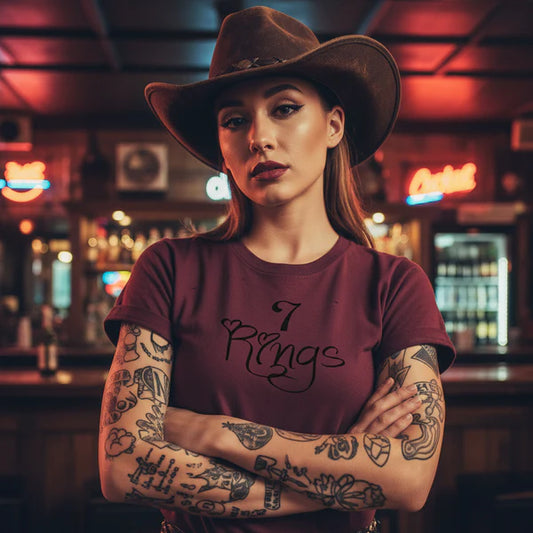 Woman wearing a maroon t-shirt with '7 Rings' design and a cowboy hat in a bar setting.