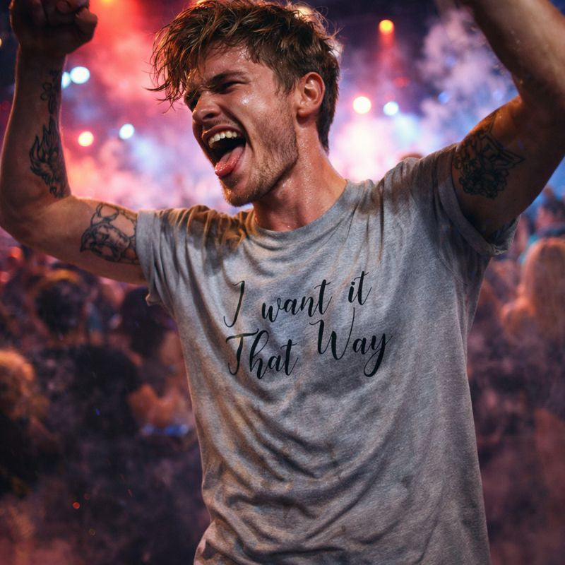Man with tattooed arms wearing a t-shirt with 'I want it That Way' text at a concert.