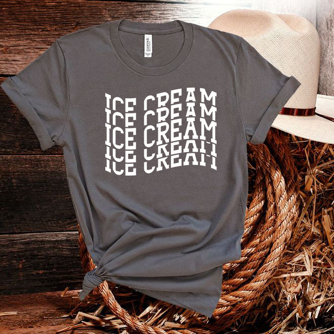 Gray t-shirt with 'ICE CREAM' text pattern on a wooden surface with a hat.