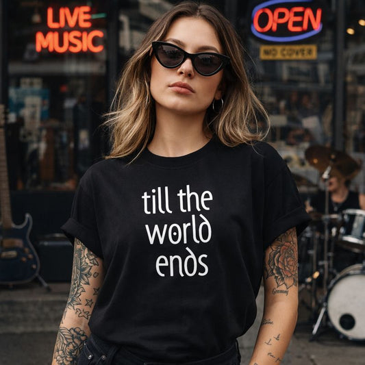 Woman wearing a black t-shirt with 'till the world ends' text in a city street setting with neon signs.