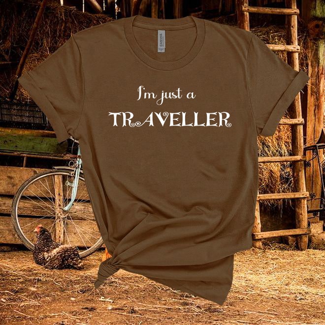 Brown t-shirt with 'I'm just a Traveller' text in a rustic setting with a chicken and bicycle.