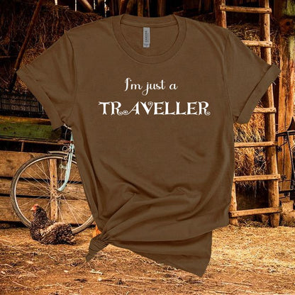 Brown t-shirt with 'I'm just a Traveller' text in a rustic setting with a chicken and bicycle.