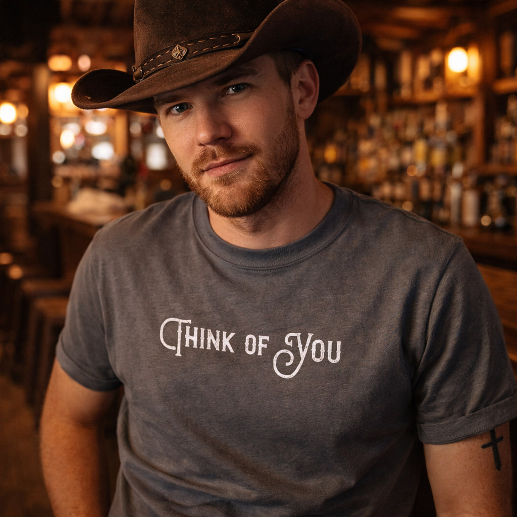 Man wearing a cowboy hat and 'Think of You' t-shirt in a bar setting