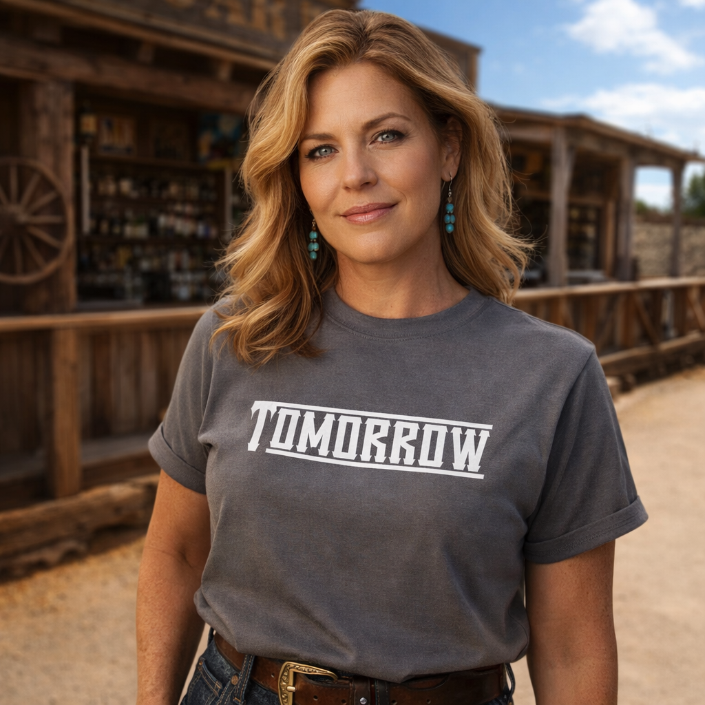 Woman wearing a gray t-shirt with 'TOMORROW' printed on it, standing in front of a wooden building.