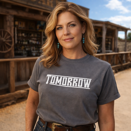 Woman wearing a gray t-shirt with 'TOMORROW' printed on it, standing in front of a wooden building.