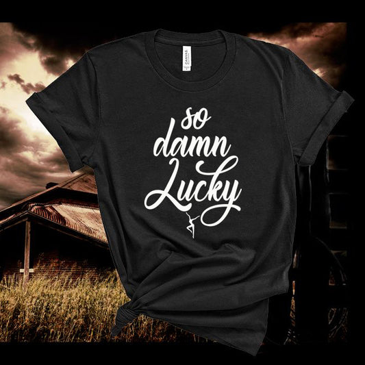 Black t-shirt with 'so damn lucky' text in white against a rustic background