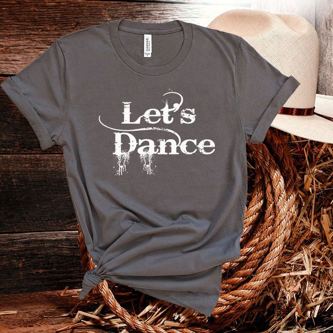 Gray t-shirt with 'Let's Dance' text on a wooden surface with a hat and basket.