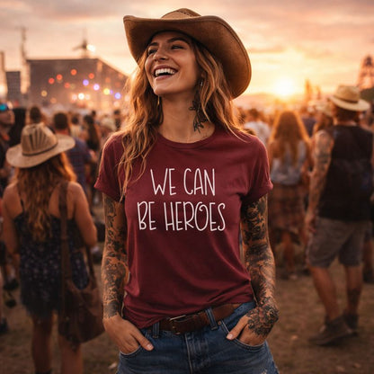Woman wearing a maroon t-shirt with 'We Can Be Heroes' at a music festival.