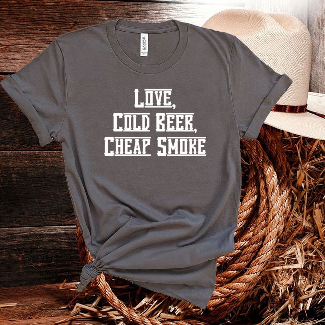 Gray t-shirt with 'Love, Cold Beer, Cheap Smoke' text on a wooden surface with a hat.