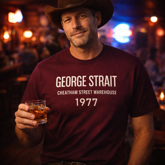 Man wearing a maroon t-shirt with 'George Strait' text, holding a glass in a bar setting.