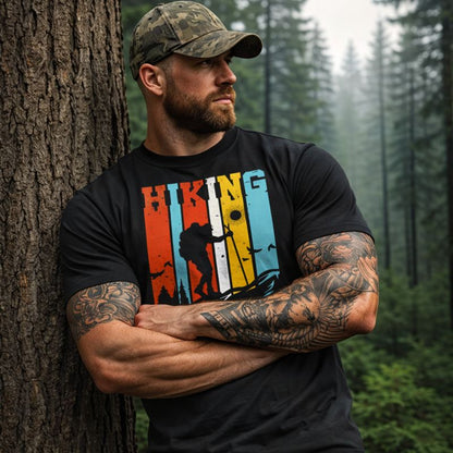 Man wearing a black t-shirt with 'Hiking' design leaning against a tree in a forest.