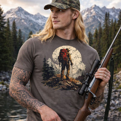Man wearing a t-shirt with a mountain and hiker design, holding a rifle in a forest setting.
