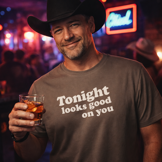 Man wearing a cowboy hat and 'Tonight looks good on you' shirt holding a drink in a bar setting.