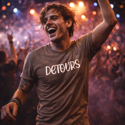 Man wearing a 'Detours' t-shirt at a concert with a crowd in the background