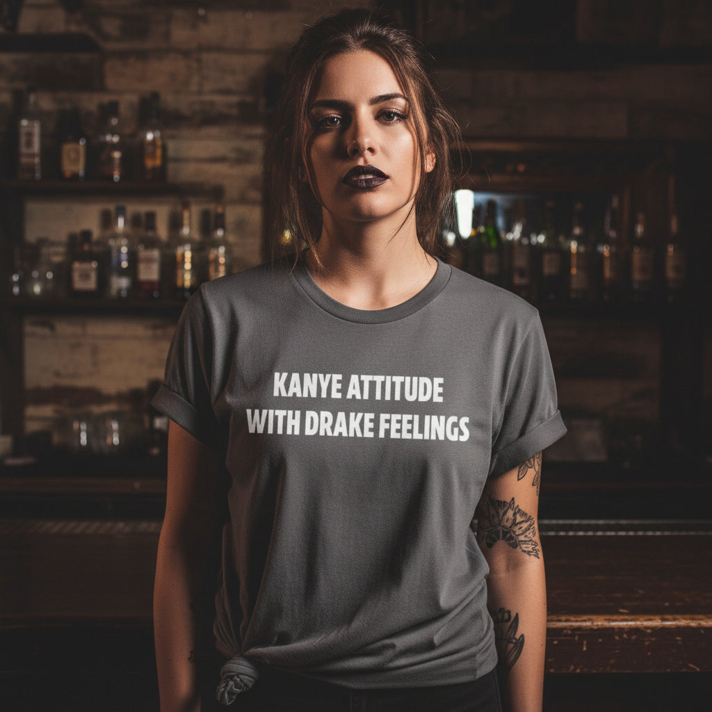Gray t-shirt with text 'Kanye attitude with Drake feelings' on a wooden surface.