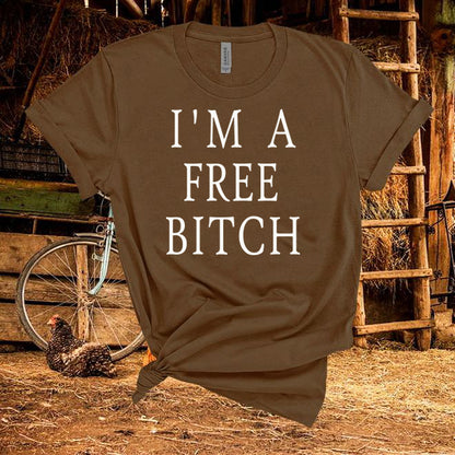 Brown t-shirt with 'I'm a Free Bitch' text in a rustic setting with a chicken and bicycle.