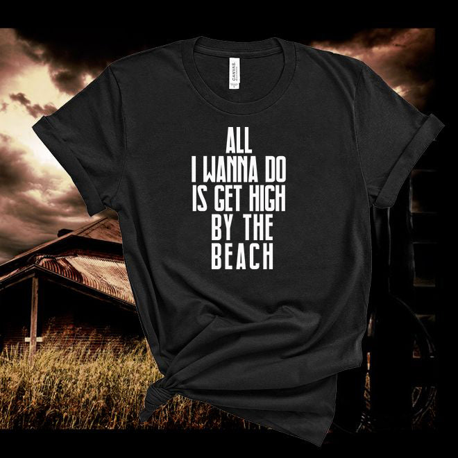 Black t-shirt with white text 'All I wanna do is get high by the beach' against a dark, moody background.