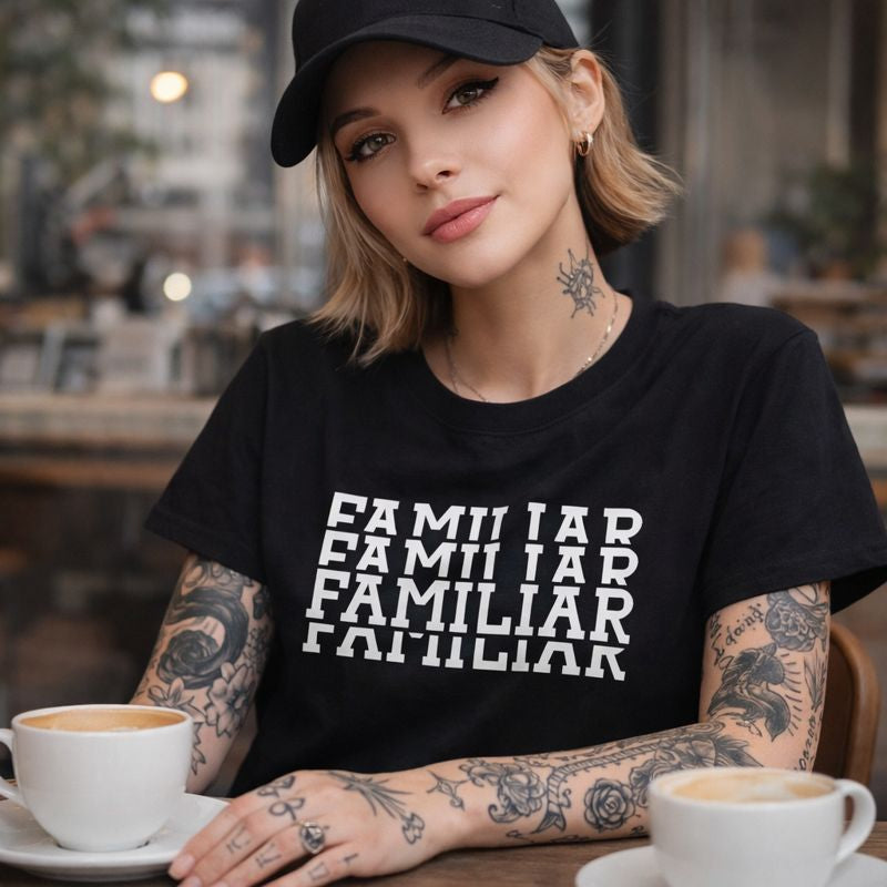 Woman wearing a black t-shirt with 'FAMILIAR' text, sitting at a table with coffee cups.
