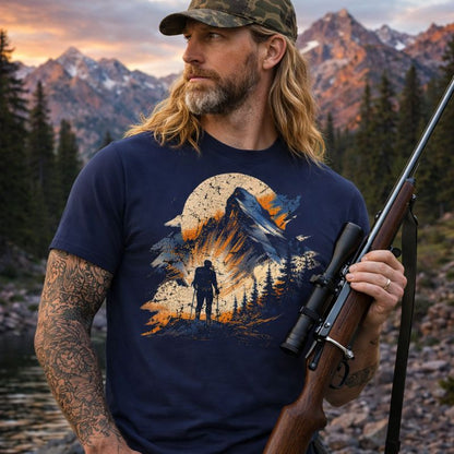 Man holding a rifle in a mountainous landscape wearing a t-shirt with a nature graphic.