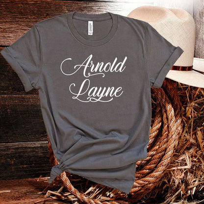 Gray t-shirt with 'Arnold Layne' text on a wooden surface with a hat and straw background
