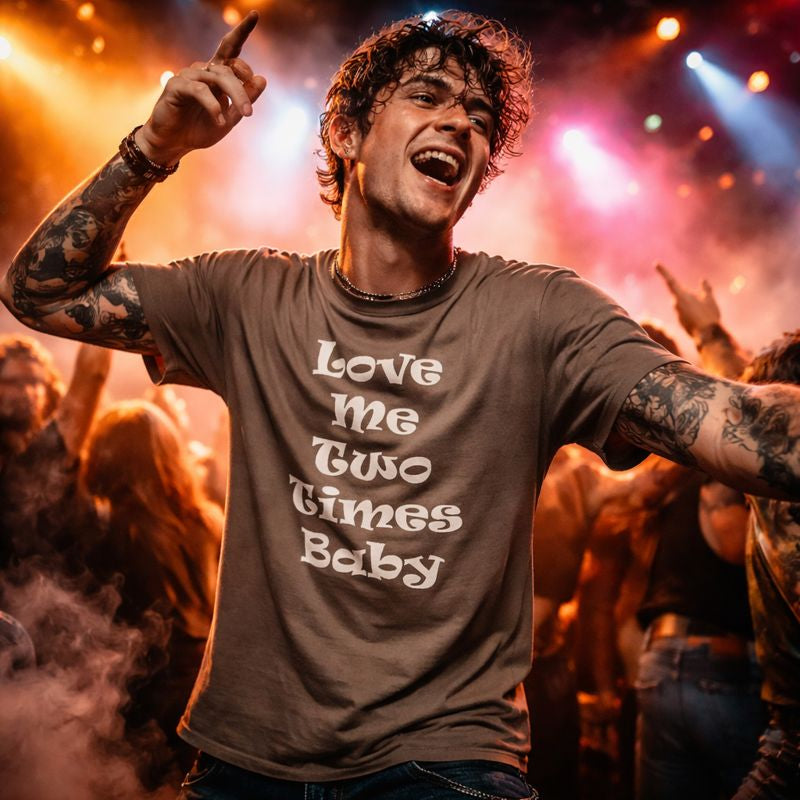 Person at a concert wearing a t-shirt with 'Love me Two Times Baby' text, surrounded by bright lights and smoke.